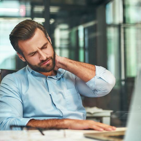 Feeling tired. Young bearded businessman in formal wear massaging his neck while sitting in the modern office. Workplace. Taking a break
